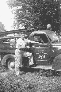 An old black and white photo of a man posing with his truck.